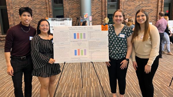 Four students stand next to their academic research poster.