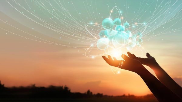 Phot of hands holding an atom in front of a sunrise