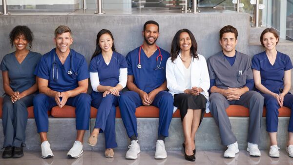 A diverse group of nurses pose together on a bench.