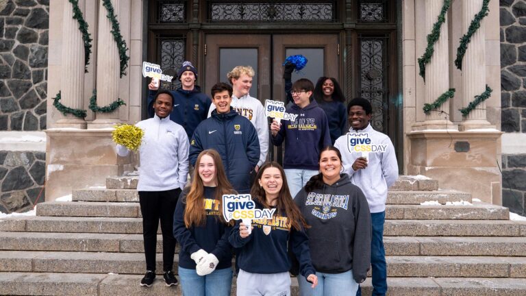 St. Scholastica students stand in front of Tower Hall with Give to CSS signs.