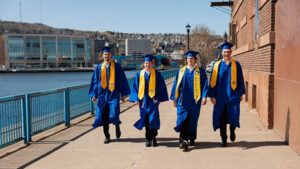 Photo of St. Scholastica's 2025 Commencement Speaker Jason Amireault walking with friends in their commencement gowns.