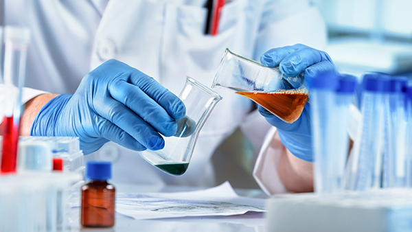 A chemist wearing blue latex gloves mixes chemicals.