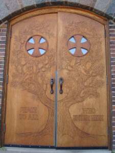 Photo of St. Scholastica's Peace Doors. The Doors feature a carved tree and the words "Peace to all who enter here"