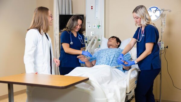 St. Scholastica students practice on a mannequin while an instructor supervises.