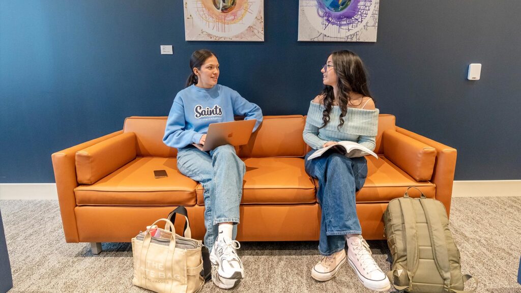 Two undergraduate St. Scholastica students chat on an orange couch in the Student Center.
