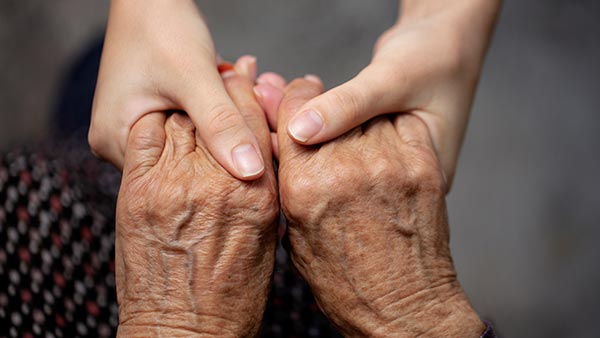 Hands of a caregiver holding the hands of an aging person.