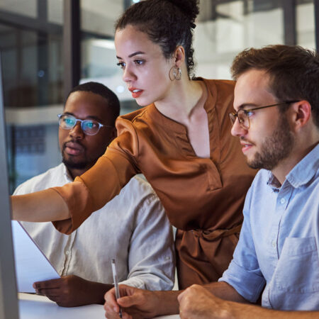 Three people working on an apple computer working through a project.