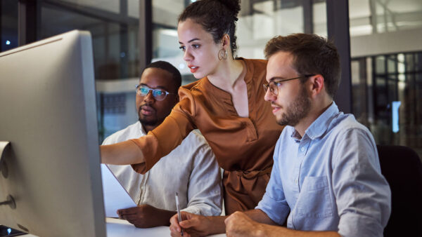 Three people working on an apple computer working through a project.