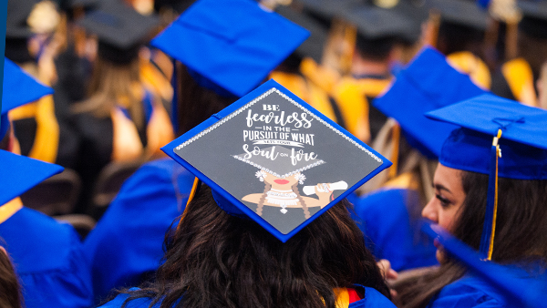 View of commencement from the back, centering on a decorated cap that says "Be fearless in pursuit of what sets your soul on fire"