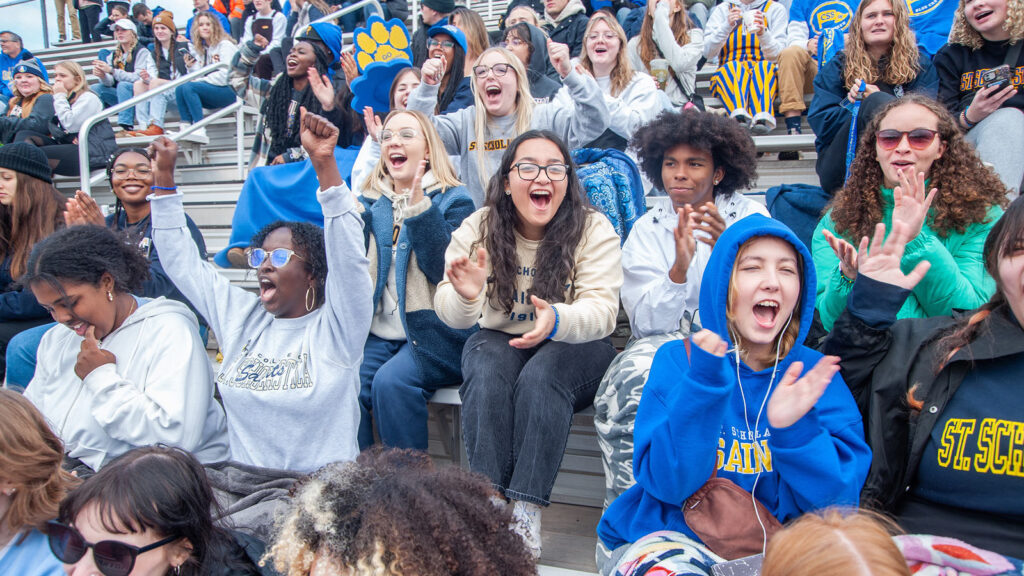 A group of students cheer on the St. Scholastica Saints during a football game.