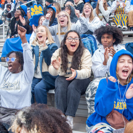 A group of students cheer on the St. Scholastica Saints during a football game.