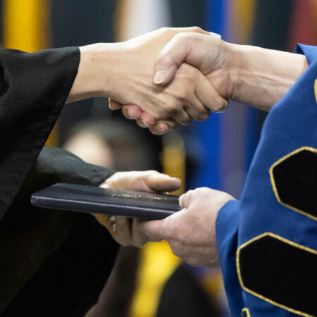 St. Scholastica leadership congratulates a new graduate during the 2026 commencement.