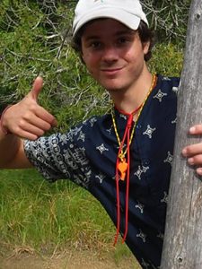 Logan Holm standing behind a tree while on a trip.
