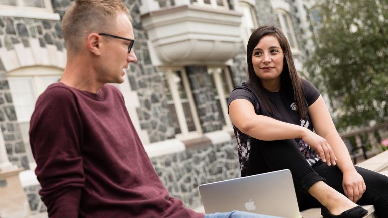 Two St. Scholastica students sitting on the steps of Tower Hall.