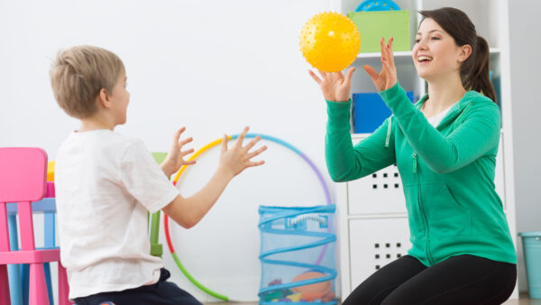 Occupational Therapist tossing a yellow ball to a young child.