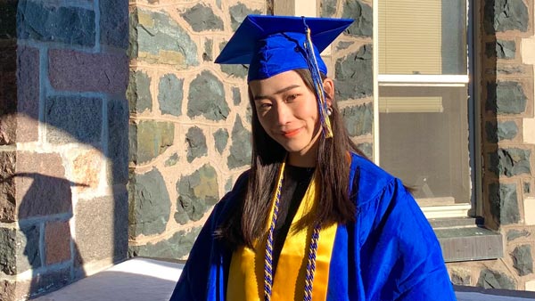 Pa Chang Vang standing by Tower Hall on the St. Scholastica campus.