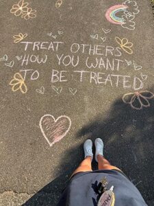 Paige Blattner with a chalk drawing that says: Treat others how you want to be treated"