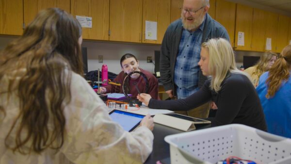Professor works with three students in a physics lab.