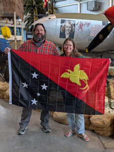 Kory Guilderman posing with a flag, posing in front of Richard Bong's plane