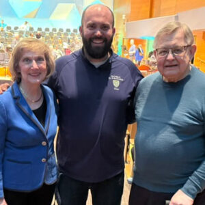 St. Scholastica's Associate Professor of Music and Director of Choral Activities, Richard Carrick standing in Orchestra hall with Sing Democracy 250's co-founders Gary Aamodt and Celia Ellingson.