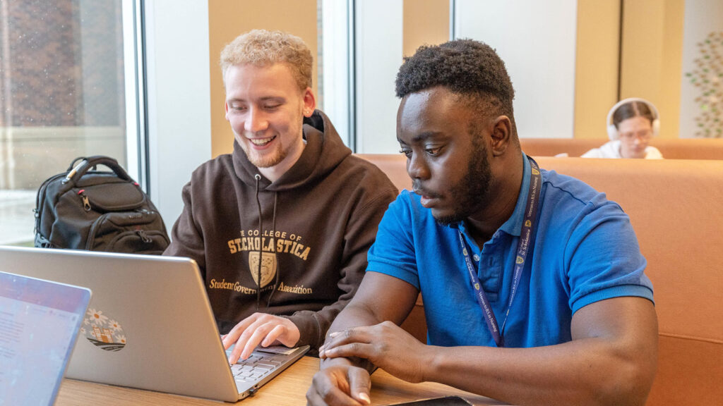 Two students sitting in St. Scholastica's Student Center, studying on a computer.