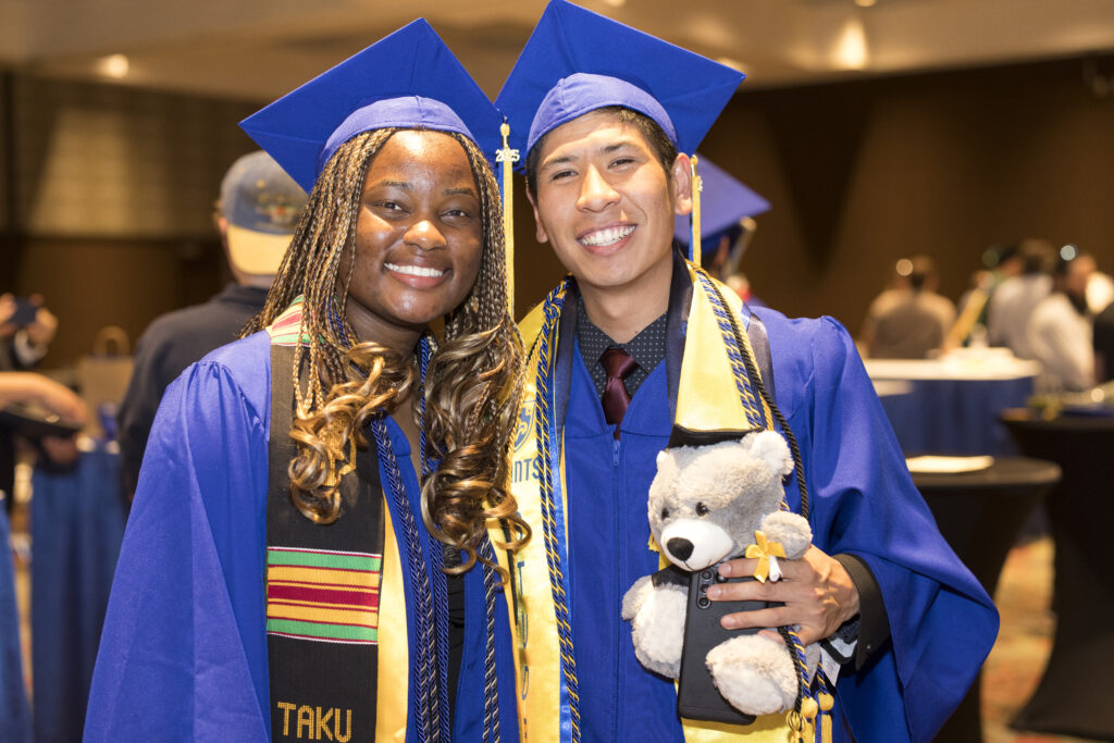 Two students dressed in graduation gear smiling.